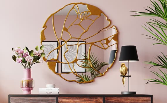 Runder Spiegel mit goldfarbenen Rahmen, reflektiert Zimmerpflanze und Bilder. Vase mit Blumen, Bücher und Lampe auf Kommode.