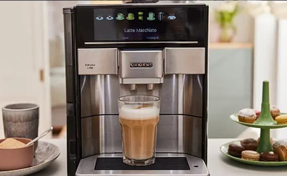 Latte Macchiato – Siemens Kaffeevollautomat bereitet Latte Macchiato zu, daneben Teller mit Zucker und Macarons auf grünem Ständer