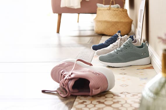 Mehrere Paar Sneaker in Pastellfarben stehen und liegen nebeneinander in einem hellen Flur