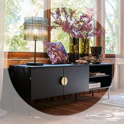 Schwarzes Sideboard vor großen Fenstern, dekoriert mit Lampe, Vasen mit Zweigen, Kissen und Büchern