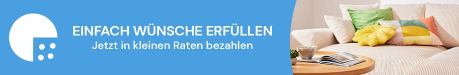 Einfach Wünsche erfüllen – Jetzt in kleinen Raten bezahlen. Helles Wohnzimmer mit beigem Sofa und bunten Kissen, daneben ein Holztisch mit Buch.