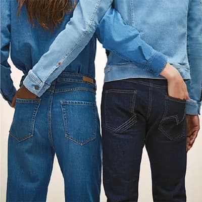 Zwei Personen in blauen Jeans und Jeansjacken stehen nebeneinander und haben die Hände in den Hosentaschen des anderen.