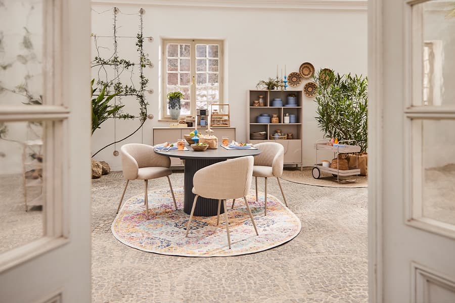 Stilvoll eingerichtetes Esszimmer mit rundem Tisch, vier Stühlen und dekorativen Pflanzen. Lichtdurchfluteter Raum.