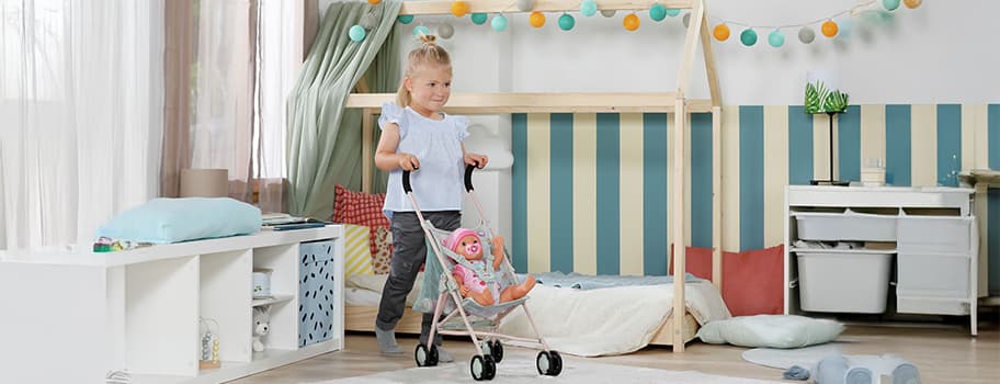 Kind in einem stilvollen Kinderzimmer schiebt einen Puppenwagen mit einer Puppe. Gemütliches Bett und farbenfrohe Dekoration.