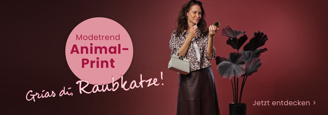 Modetrend Animal-Print – Frau im Leo-Muster-Jacke mit Tasche steht neben Deko-Pflanzen vor rotem Hintergrund
