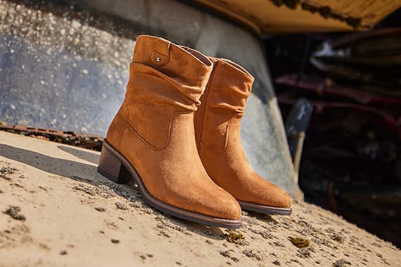 Hellbraune knöchelhohe Stiefeletten mit Blockabsatz stehen im Freien auf sandigem Untergrund