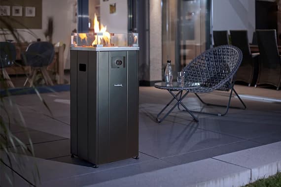 Gartenfeuer auf hoher rechteckiger Säule neben runder Sitzgruppe auf moderner Terrasse bei Abenddämmerung