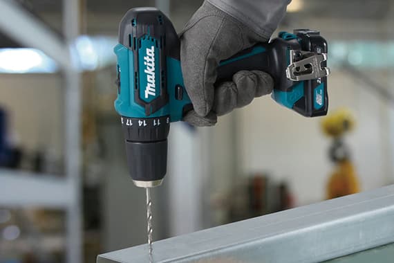 Makita Akku-Bohrschrauber in behandschuhter Hand bohrt ein Loch in ein Metallprofil in einer Werkstatt