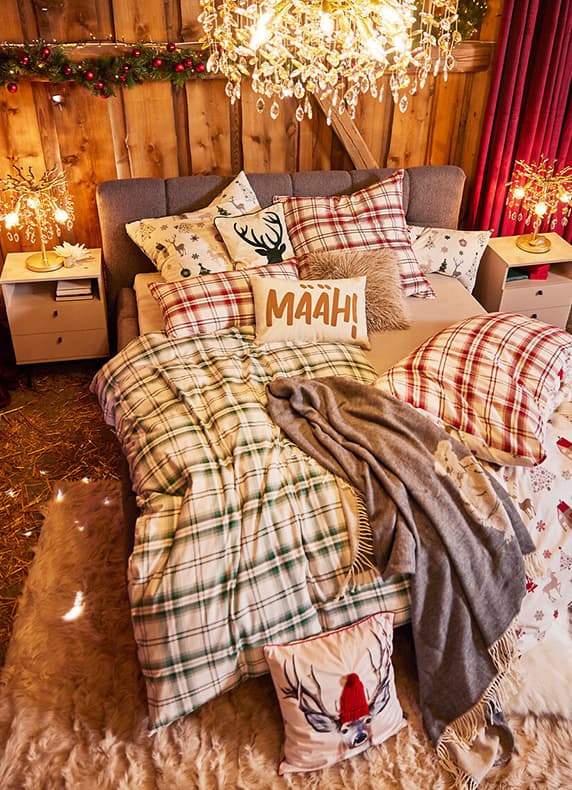 Kissen mit Aufschrift MÄÄH! auf weihnachtlich dekoriertem Bett mit Karobettwäsche und Rentiermotiven in gemütlichem Schlafzimmer