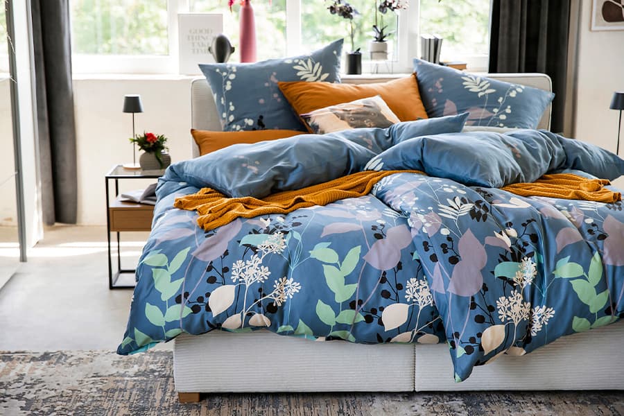 Bett mit blauer Bettwäsche, bunten Kissen und natürlichem Licht.