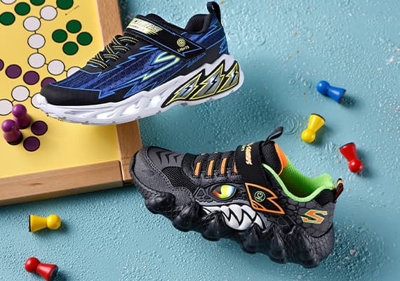 Zwei Paar Kindersneaker – ein blaues Paar mit Blitzmuster, ein schwarzes Paar mit Monsterdesign, daneben bunte Spielfiguren und Spielbrett.
