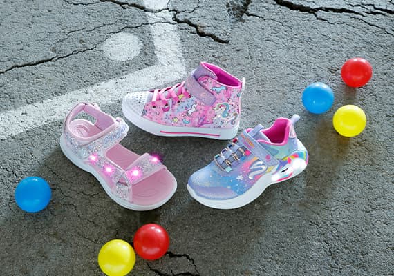 Drei Paar Kinderschuhe in rosa und lila Farben, umgeben von bunten Bällen auf Asphalt