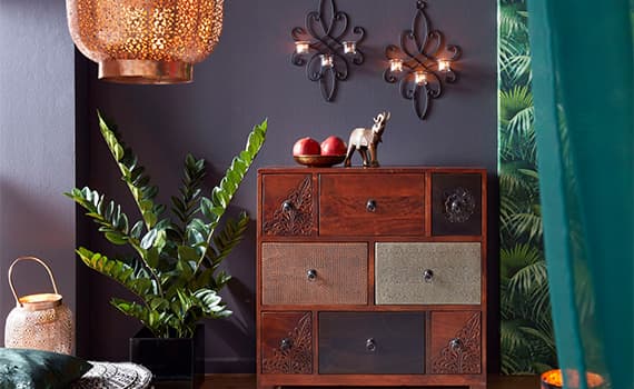 Wohnzimmer mit brauner Kommode, grüner Pflanze, zwei roten Äpfeln und einem goldenen Ziergegenstand auf der Kommode
