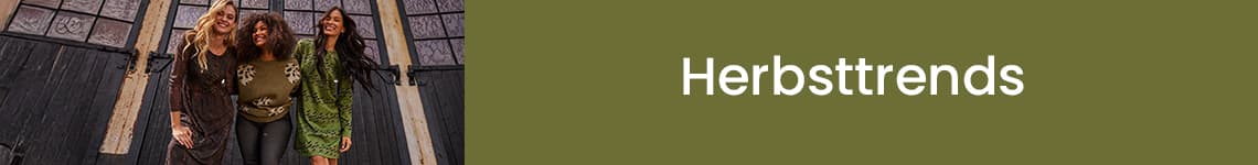 Herbsttrends – Drei Frauen in Herbstmode stehen zusammen vor einem Gebäude mit großen Fenstern