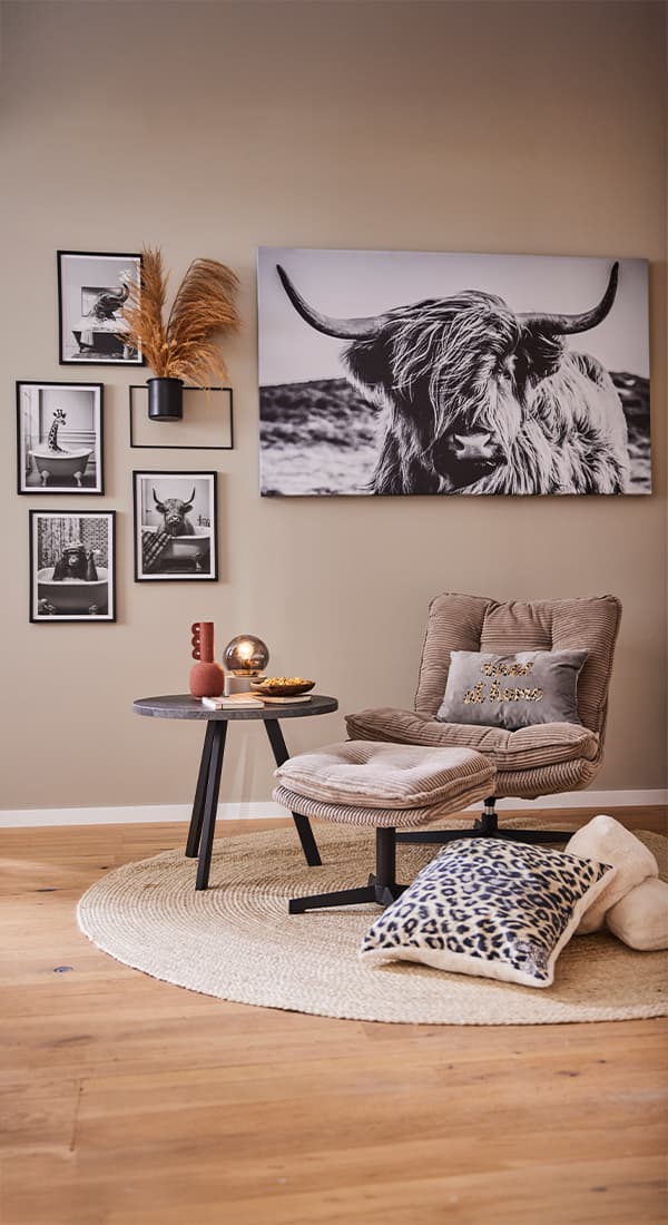 Sessel mit grauem Kissen und Tisch auf Teppich, Wandbilder von Tieren, darunter ein großes Bild von einem Hochlandrind