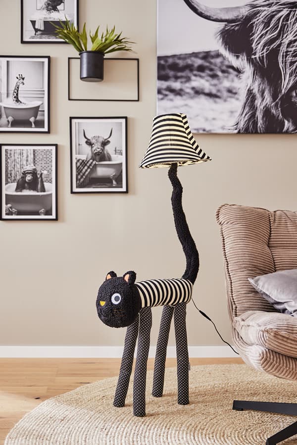Wohnzimmer mit Wandleuchten in Form eines Katzenkörpers, schwarz-weiß gestreift, daneben gerahmte Tierbilder und Topfpflanze