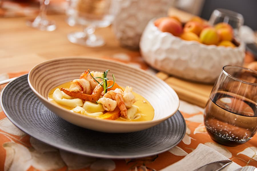 Schüssel mit Garnelen und Gemüse auf einem gedeckten Tisch, daneben ein Glas Wasser und eine Schale mit frischem Obst