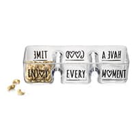 Schale mit den Worten "ENJOY EVERY MOMENT" und Herzsymbolen, gefüllt mit Cashewnüssen, daneben liegen einige Nüsse.