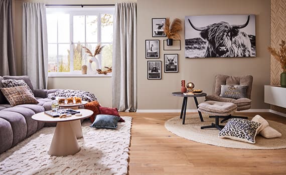 Modernes Wohnzimmer mit grauem Sofa und Sessel, dekoriert mit bunten Kissen, Teppichen und Bildern, darunter eine Abbildung eines Stiers.