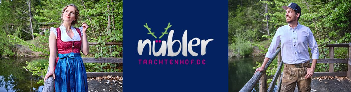 Nübler Trachtenhof – Frau in rotem Dirndl mit blauem Rock und Mann in weißem Hemd mit Lederhose auf Holzbrücke im Wald