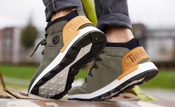 Person trägt graue Timberland-Sneaker mit braunen Details, zeigt die Sohlen beim Gehen auf einer metallischen Oberfläche.