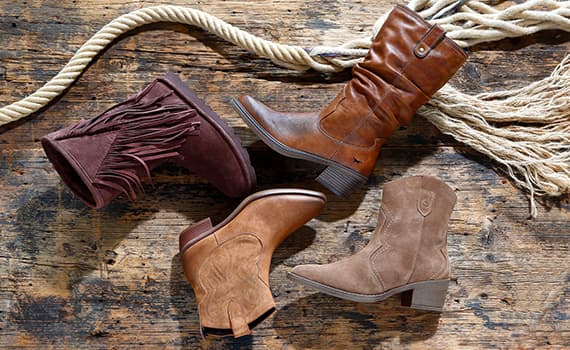 Vier verschiedene Paar braune Stiefel liegen auf einem rustikalen Holzboden mit einem Seil im Hintergrund