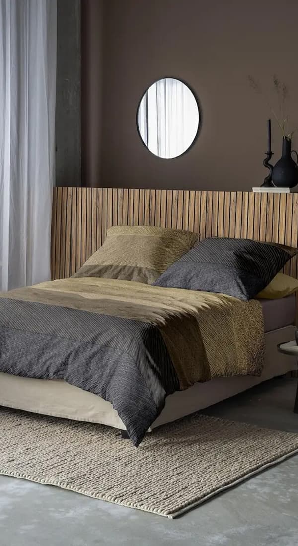 Doppelbett mit gestreifter Bettwäsche, runder Spiegel an der Wand, Holzrückwand, Vorhänge und Teppich im Schlafzimmer