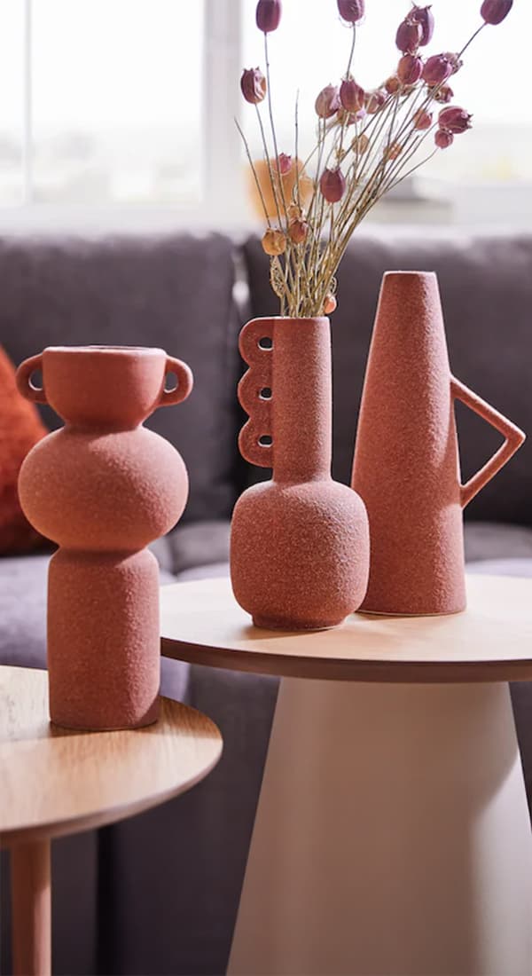 Drei braune Vasen in verschiedenen Formen stehen auf einem runden Tisch, eine davon ist mit getrockneten Blumen gefüllt.