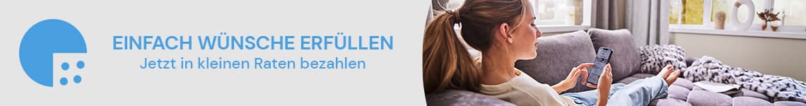 EINFACH WÜNSCHE ERFÜLLEN – Frau liegt auf Sofa und hält Smartphone, Wohnzimmer mit grauem Sofa und Fenster im Hintergrund