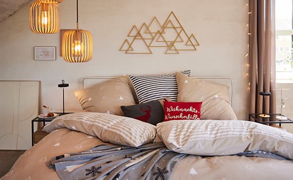 Weihnachtswunschkissen – gemütliches Schlafzimmer mit festlicher Bettwäsche, zwei Lampen, Wanddeko und einem Fenster mit Vorhängen