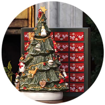 Weihnachtsbaum aus Keramik mit bunten Figuren und Stern an der Spitze, davor Adventskalender mit roten und weißen Schneeflockenmuster-Schubladen