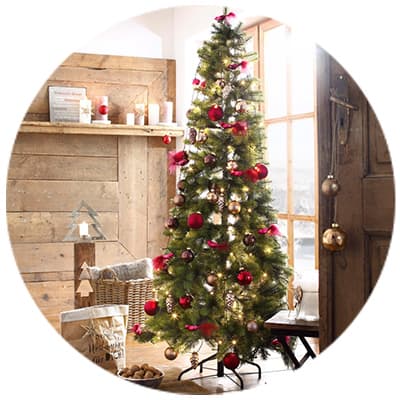 Weihnachtsbaum mit roten und goldenen Kugeln, dekoriert mit Federn, steht in rustikalem Raum mit Holzverkleidung und Kerzen