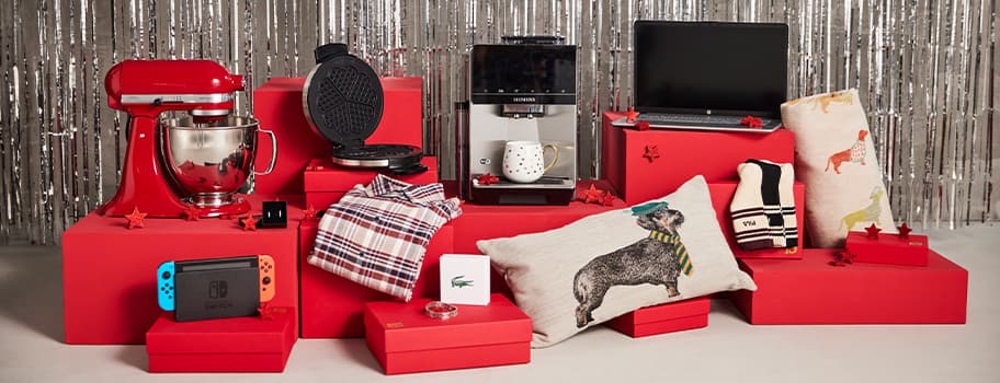 Verschiedene Geschenkideen auf roten Podesten, darunter Küchenmaschine, Waffeleisen, Kaffeemaschine, Laptop, Kleidung, Kissen und Nintendo Switch