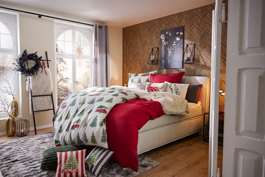 Weihnachtlich dekoriertes Schlafzimmer mit Bettwäsche im Tannenbaum-Design, roten Kissen und weihnachtlichen Accessoires