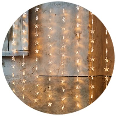 Sternförmige Lichterketten hängen vor einer rustikalen Wand und leuchten warm.