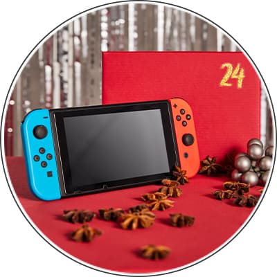 24 – Nintendo Switch mit blauem und rotem Joy-Con vor rotem Geschenk und weihnachtlicher Dekoration
