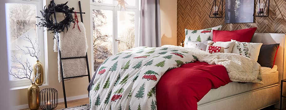 Festlich dekoriertes Schlafzimmer mit Weihnachtsbettwäsche, rotem Bettbezug und Kissen, Winterlandschaft durch Fenster sichtbar