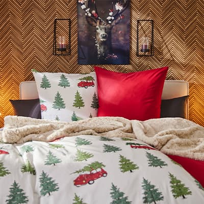 Gemütliches Schlafzimmer mit Weihnachtsbettwäsche, roten und schwarzen Kissen, und einem Hirschbild an der Wand.