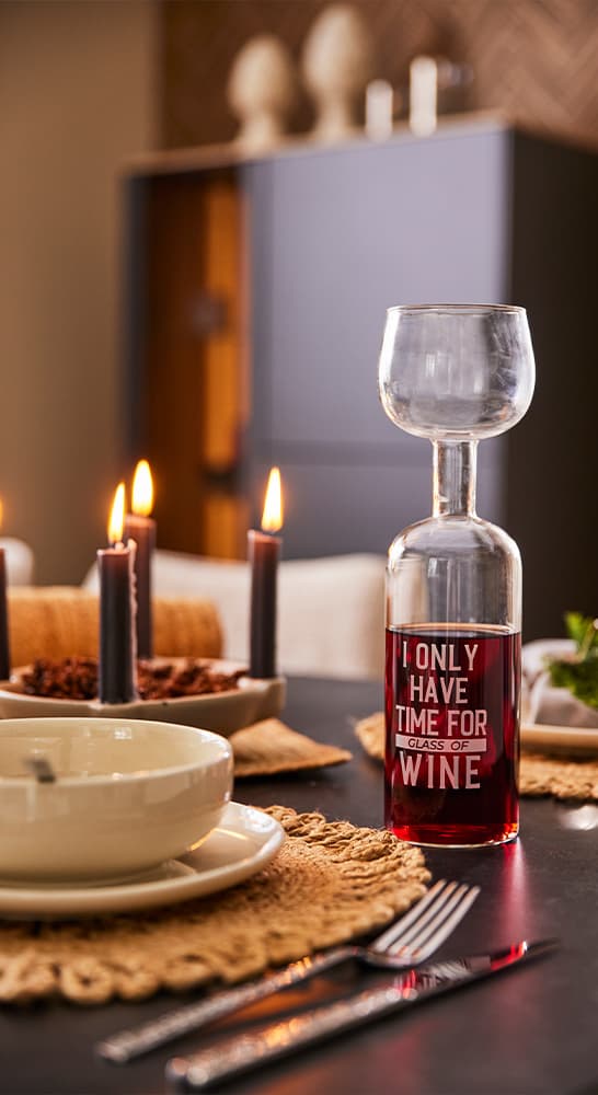 I ONLY HAVE TIME FOR GLASS OF WINE – gedeckter Tisch mit Kerzen, Teller und Besteck, im Hintergrund ein Schrank