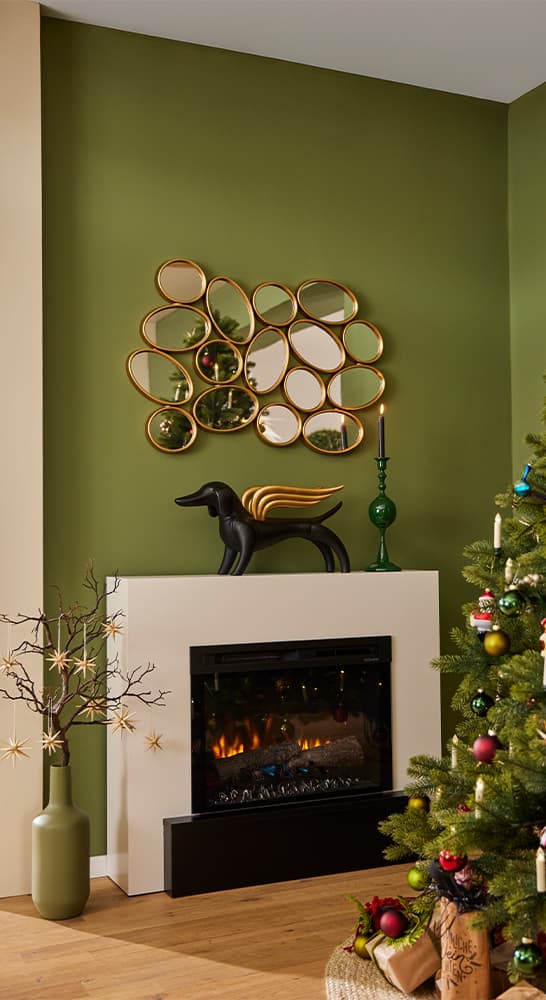 Weihnachtlich dekoriertes Wohnzimmer mit grünem Baum, Kamin, schwarzer Hundeskulptur, grüner Vase und goldenen Spiegeln an der Wand.