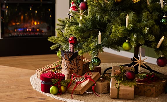 Weihnachtsbaum mit bunten Kugeln und Geschenken darunter, im Hintergrund ein Kamin mit Feuer