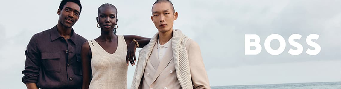 BOSS - Drei Personen stehen am Strand in stilvoller Kleidung, eine Frau in cremefarbenem Top und zwei Männer in Jacken.