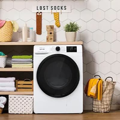 Waschmaschine in einem ordentlichen Waschraum, Schild "Lost Socks" darüber, Korb mit Wäsche und Regale mit Handtüchern.