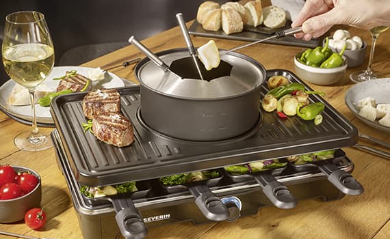 Severin Raclette-Grill mit Fondue-Topf, Fleisch, Gemüse und Brot auf dem Tisch, Hand taucht Brotstück in Käsefondue