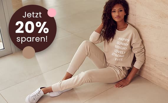 Jetzt 20 % sparen! Frau in beige Jogginganzug mit Schriftzug sitzt auf dem Boden.