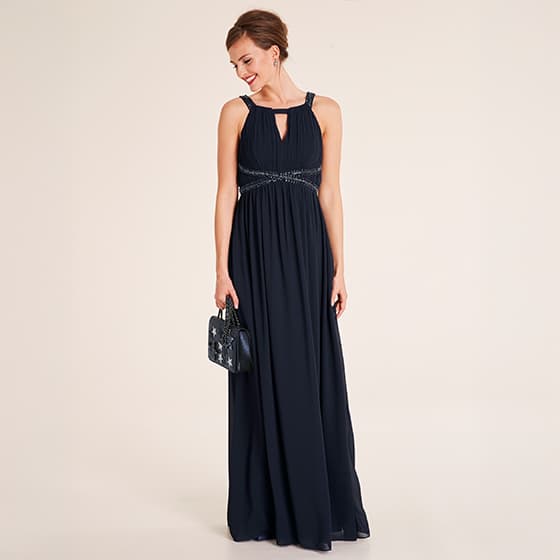 Frau in langem, dunklem Abendkleid mit Schmuckdetails und kleiner Handtasche.