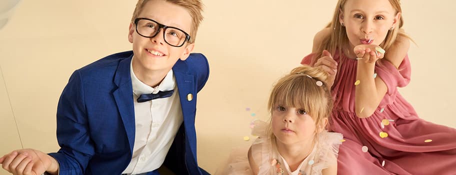 Kinder werfen Konfetti, Junge im blauen Anzug, Mädchen in rosa Kleidern lächeln und sitzen zusammen.