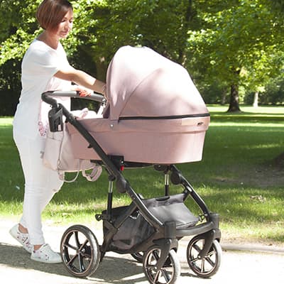 Person schiebt rosa Kinderwagen im Park.