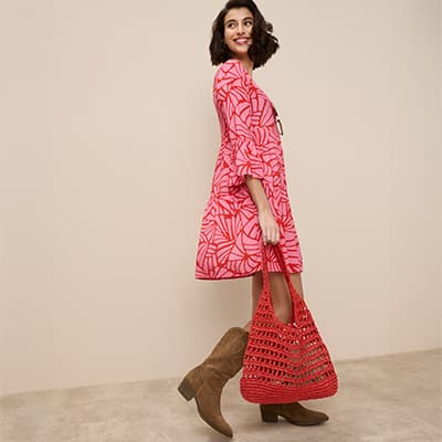 Frau in rotem Kleid mit Muster trägt rote Tasche und braune Stiefel.