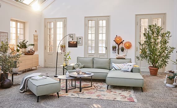 Modernes Wohnzimmer mit grünem Sofa, Beistelltischen, Pflanzen und Dekorationen vor weißen Wänden und Doppeltüren.